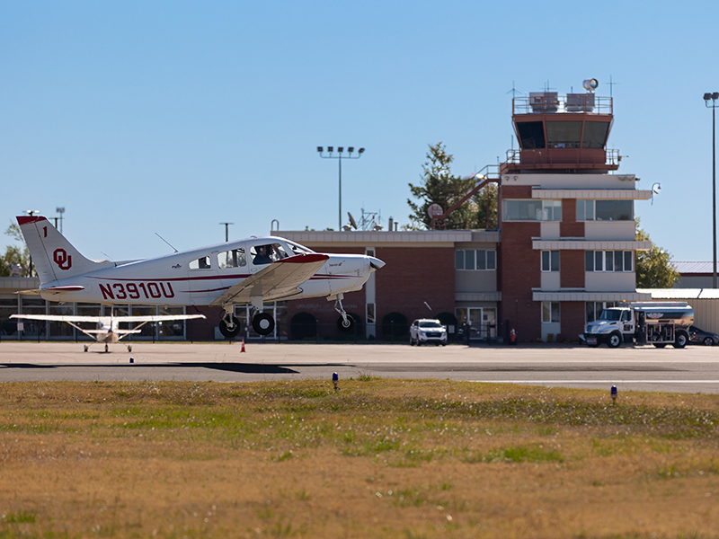 An OU airplane parked in front of the airport control tower.