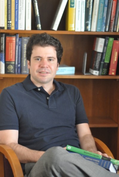 A photo of Bruno Uchoa sitting in front of a bookcase.