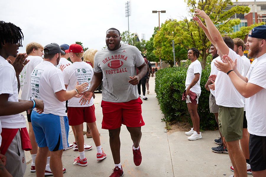A student in and OU Football t-shirt gives high fives to a crowd of fellow students.