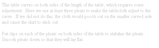Text Box: This table curves on both sides of the length of the table, which requires some adjustment.  Here we use at least three pleats to make the tablecloth adjust to the curve.  If we did not do this, the cloth would pooch out on the smaller curved side and cause the skirt to stick out.
Put clips on each of the pleats on both sides of the table to stabilize the pleats.  Smooth pleats down so that they will lay flat.
