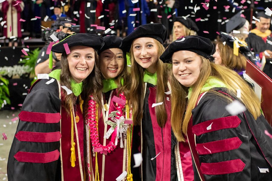 Four students in graduation regalia with confetti in the air. 
