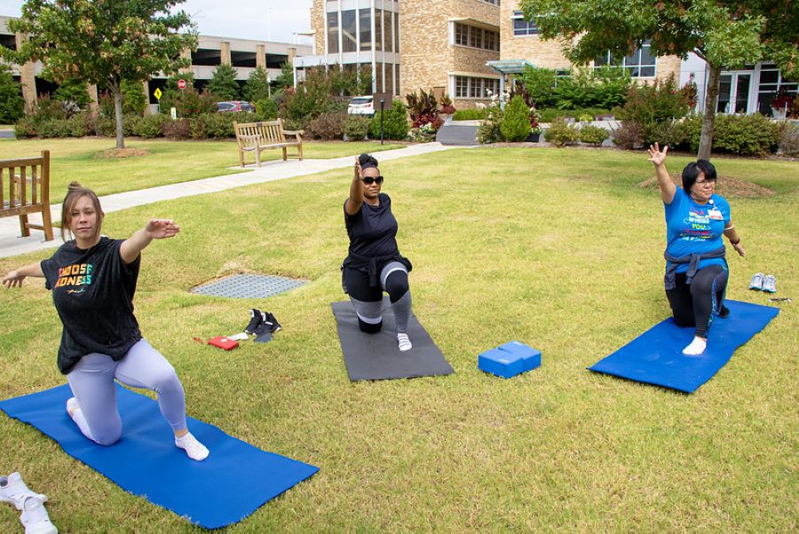 Three students doing yoga on grass with building in the background. 