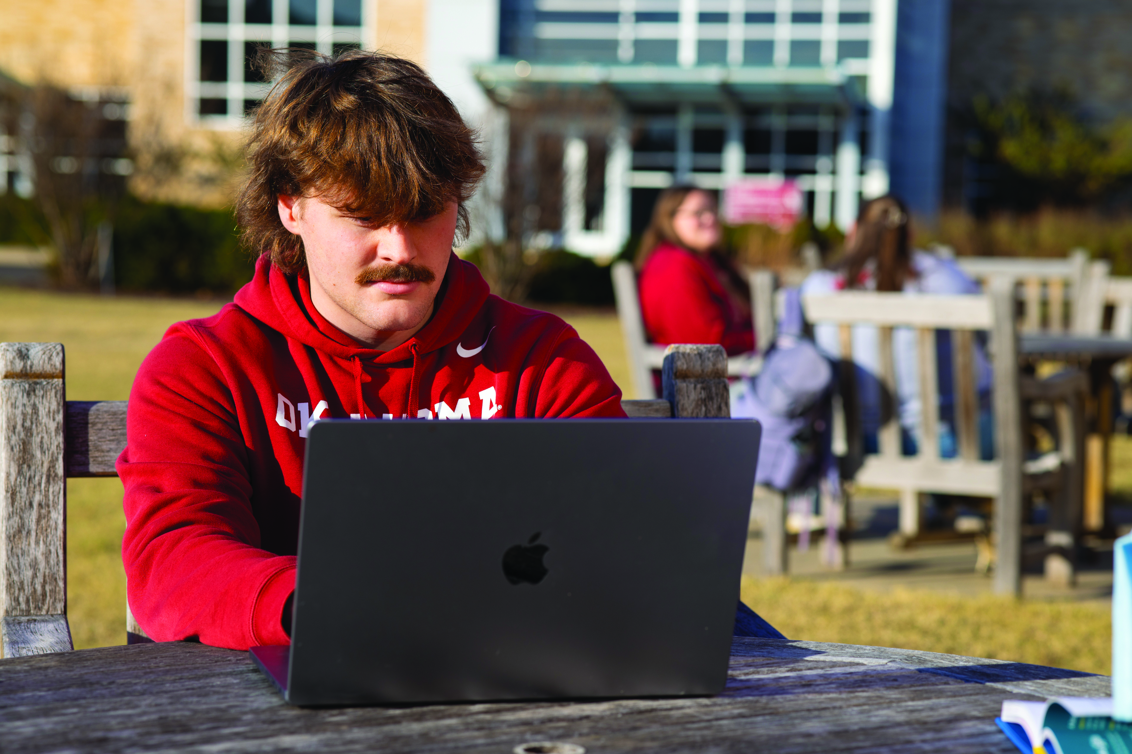 OU-Tulsa student sits outside and looks at a laptop screen.