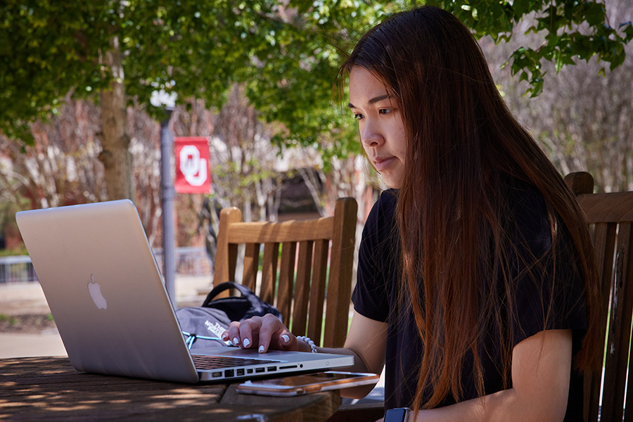 A young student working at a laptop while sitting outside.