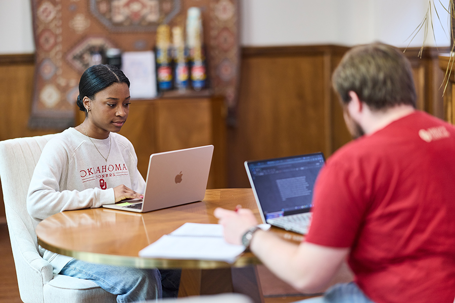 Two students sitting at a table, working on laptops.