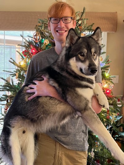 A photo of Adam Moss holding his black and white dog.