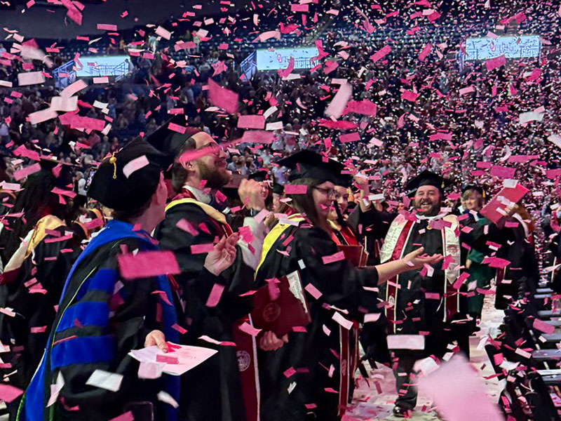 Red and white confetti falls around faculty and graduating students. 