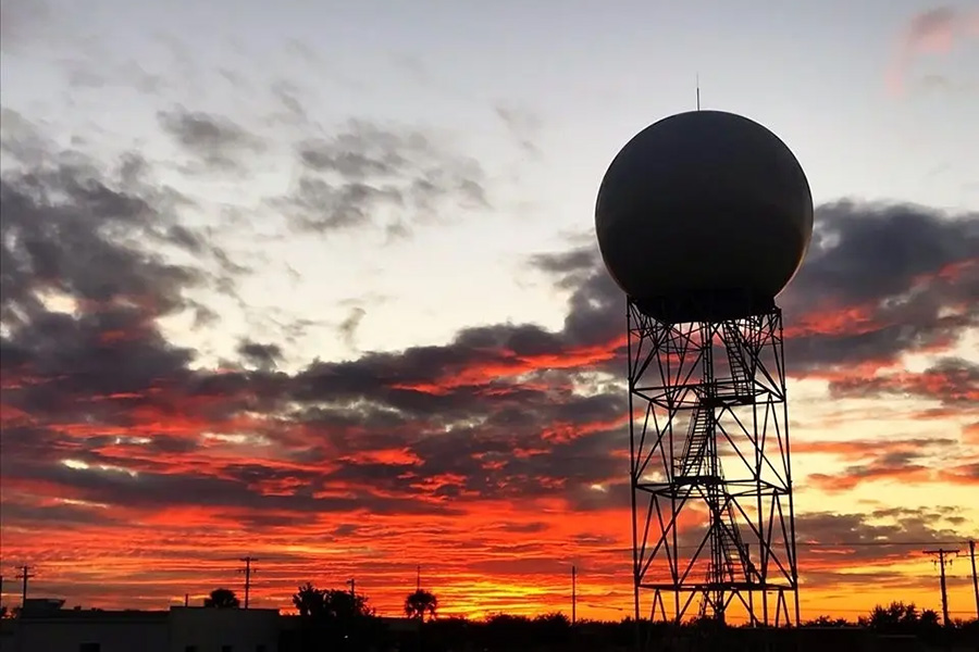 A NEXRAD radar tower stands tall with a red and yellow sunset behind it.