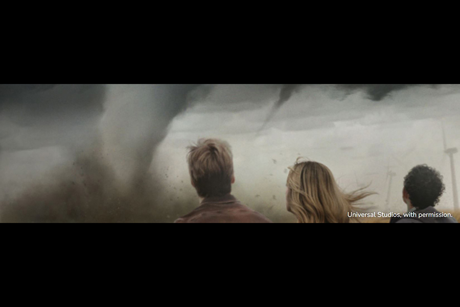 Three people with their backs turned, looking at a tornado in the sky.