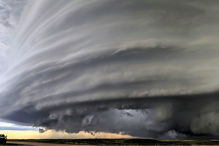 A gray swirling storm encompasses the landscape while a truck, small in comparison, is nearby.