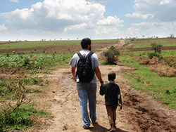 Man and boy walking across African field.