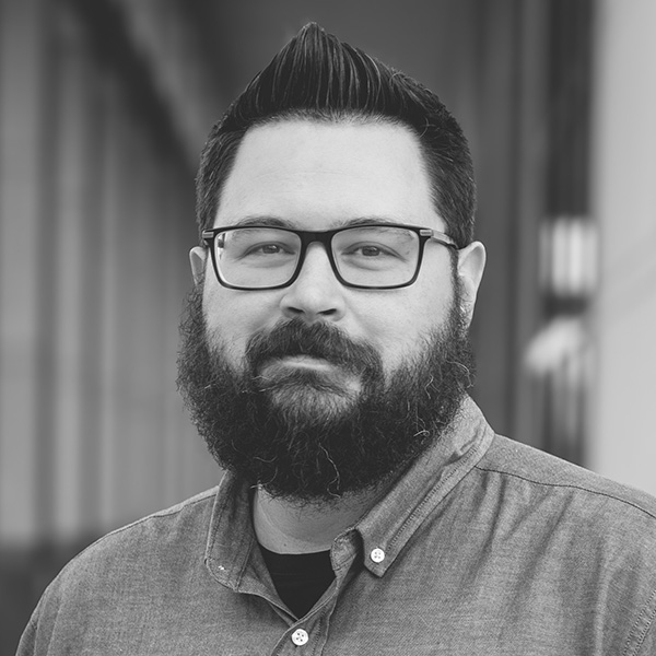 man in button up shirt, dark hair and beard; glasses