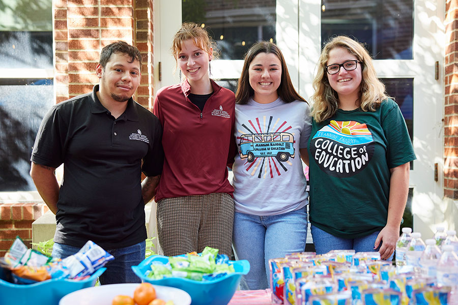 a group of four students stand at a table of refreshments during student orientation.
