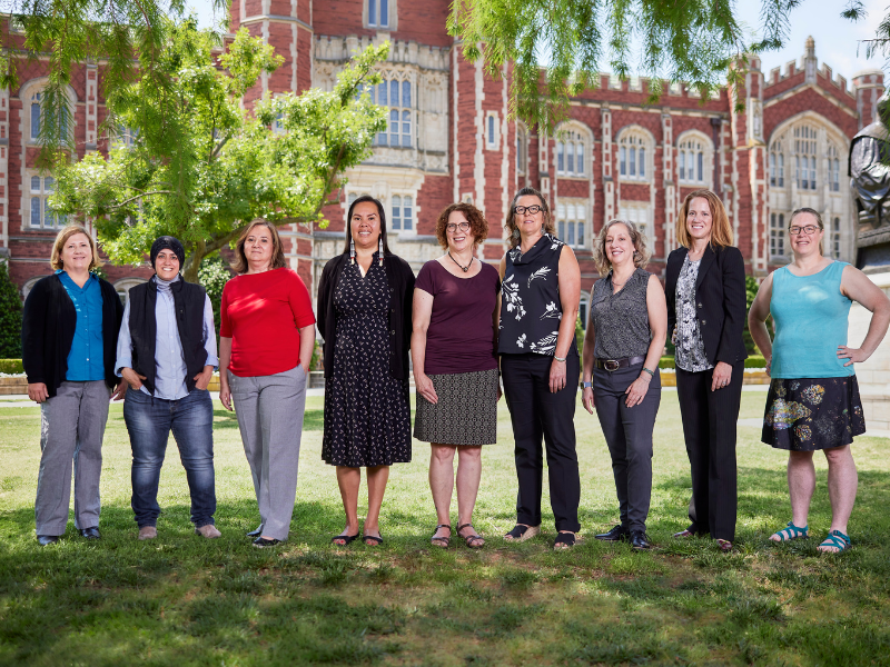 nine women standing together in front of a red brick building posing for a picture