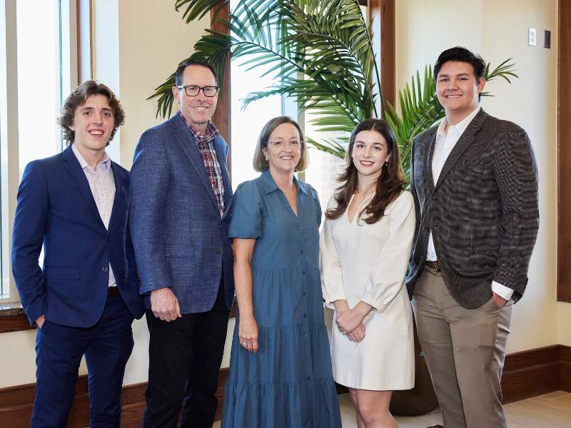 Two women and three men standing in front of a plant for a group photo