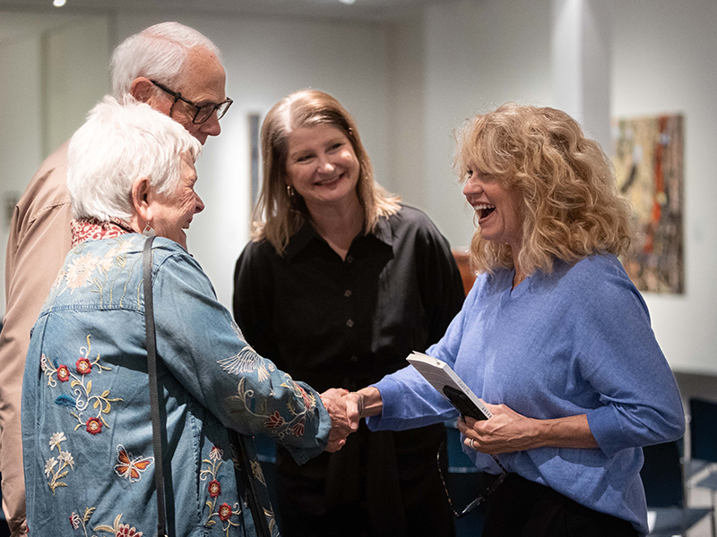 Woman in blue shirt shaking hands with woman in teal shirt as another man and woman look on