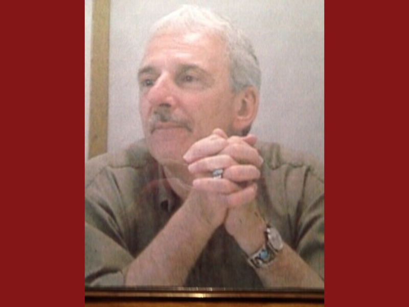 Man in a brown shirt sitting with his hands folded by his chin