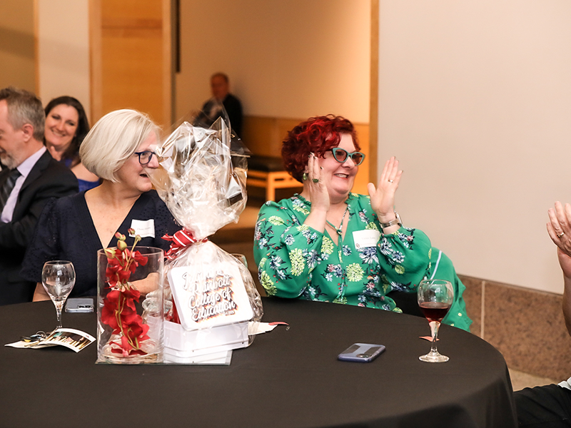 Two women sitting at a table smiling and clapping