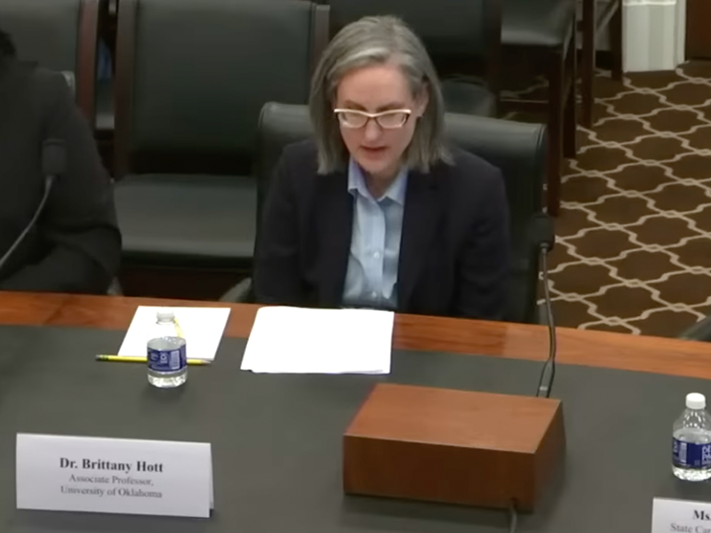Woman in a black jacket and blue shirt sitting at a table in front of a microphone