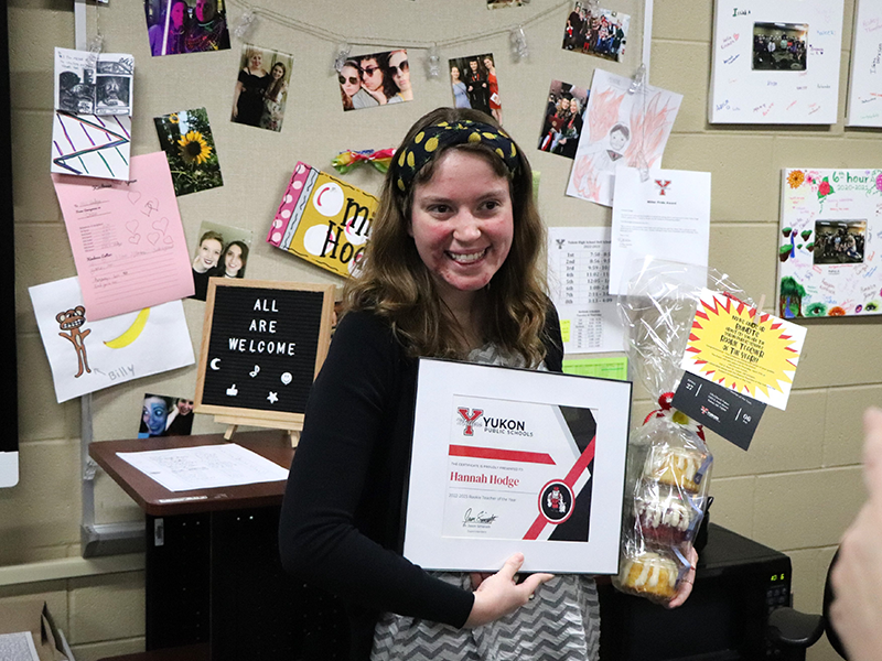 Woman in black top with headband standing in front of a bulletin board holding an award