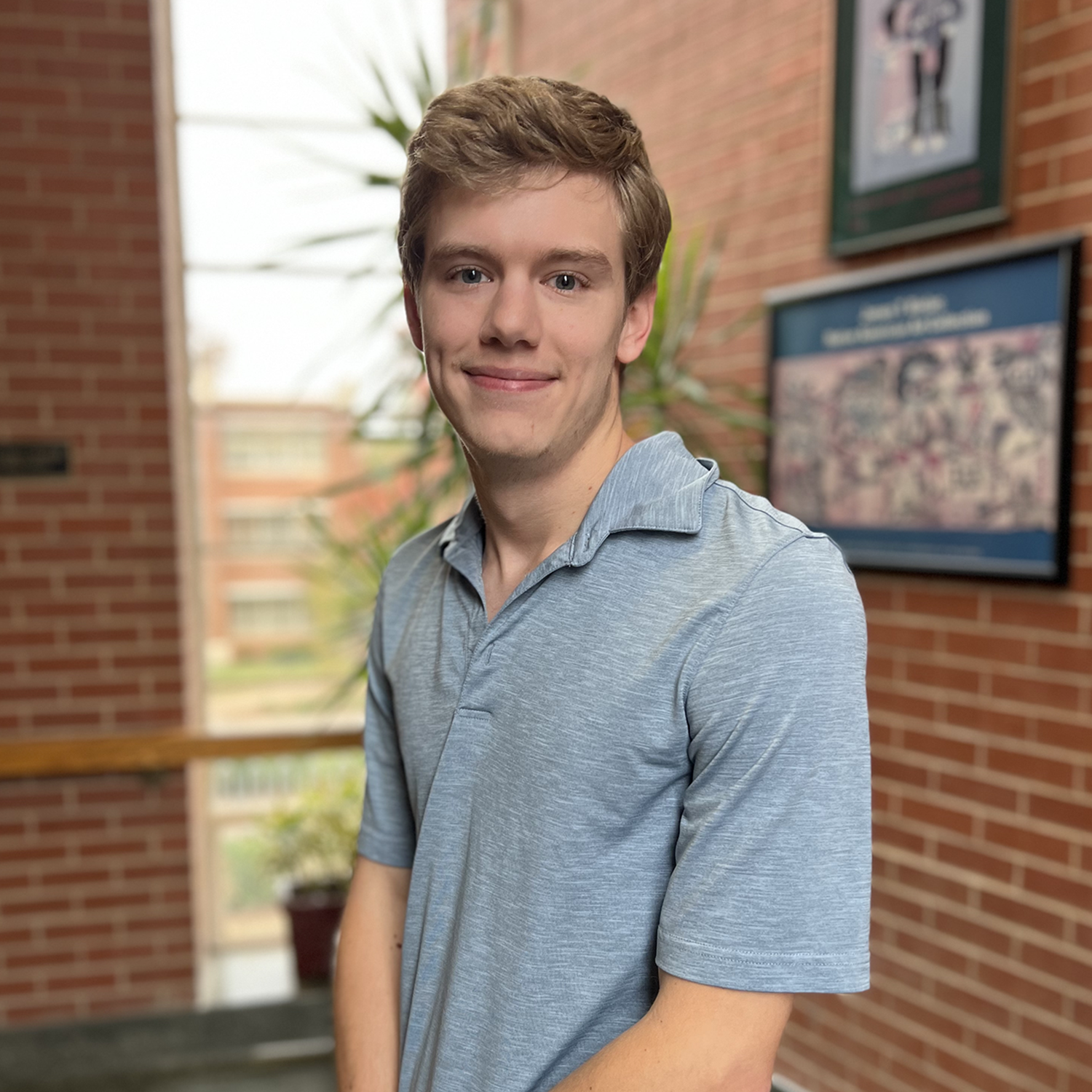 a man in a blue/gray short sleeved polo shirt standing in front of a brick wall