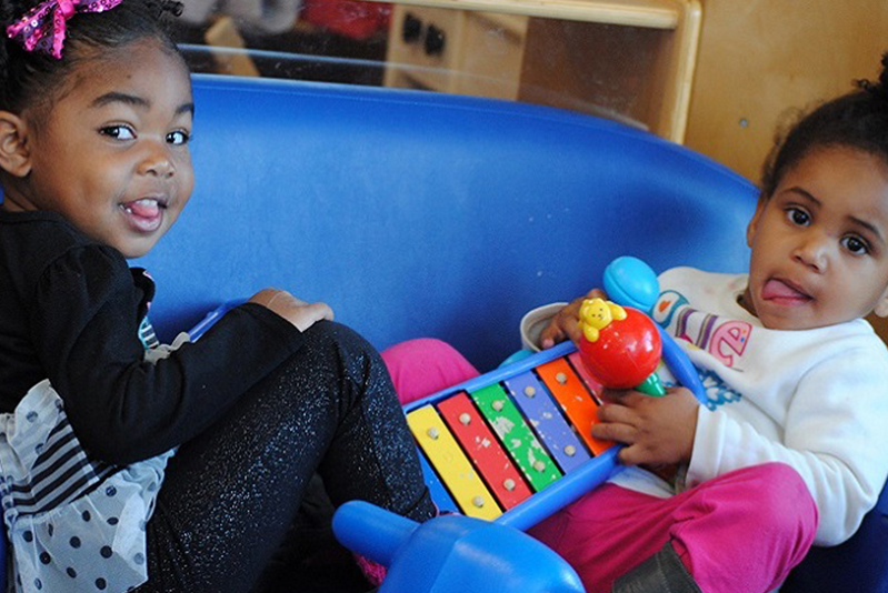Two small children sitting on blue couch playing with a toy