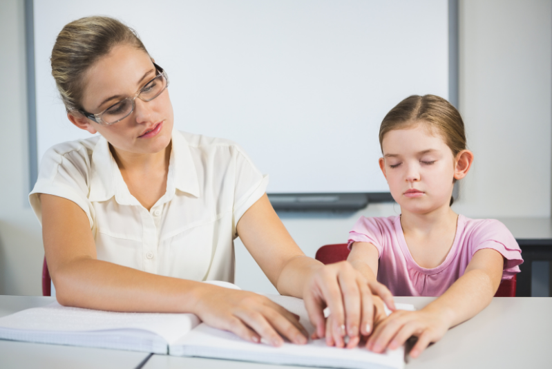 Teacher helping a blind student with braille