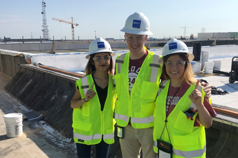 Three students in hardhats and yellow construction vests.