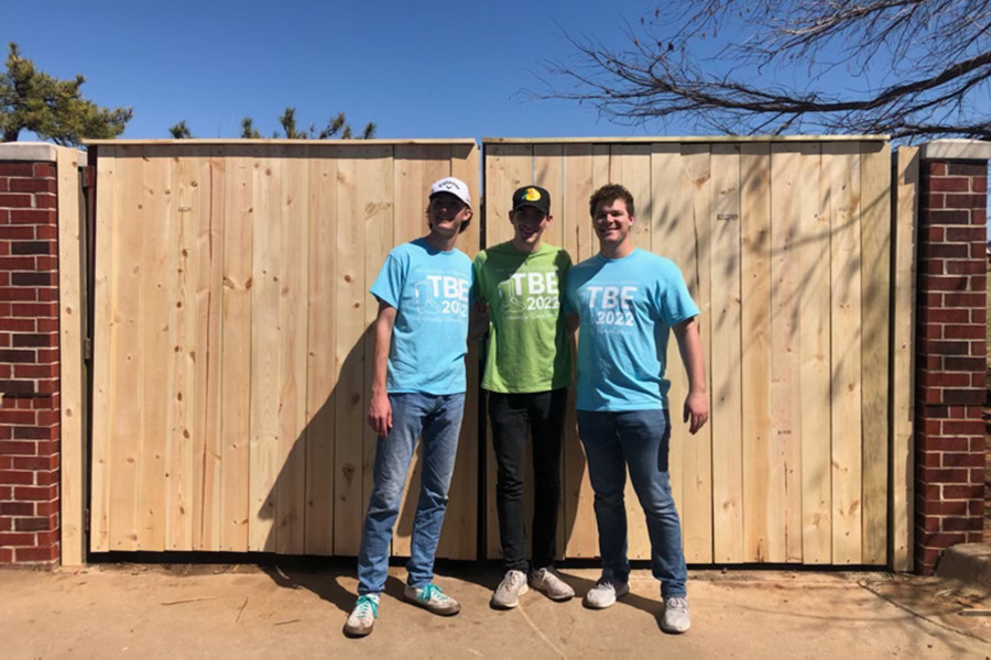 Three students posing for a photo in front of a newly constructed fence.