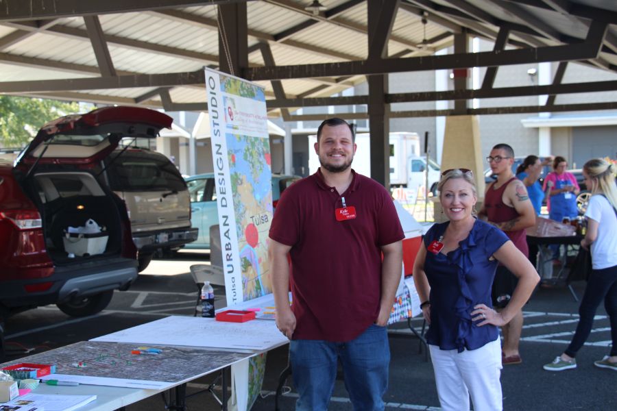 Two individuals stand under a metal roof in front of a poster display