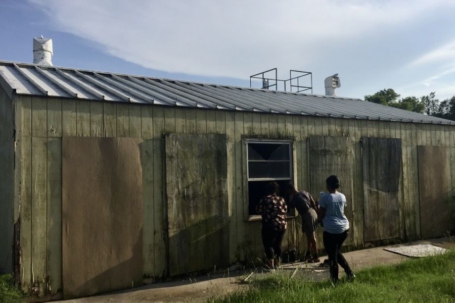 Three people looking through window of weathered building with boarded walls