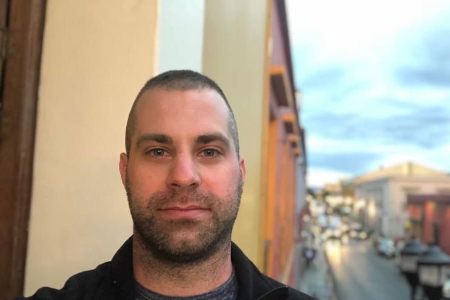 Headshot of a man on a patio balcony with a busy street underneath