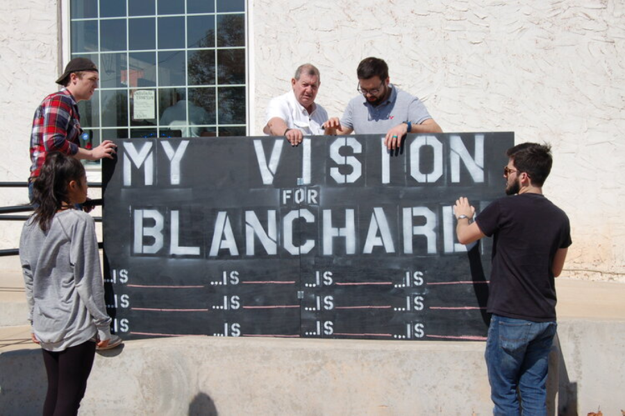 People installing a sign that says "my vision for Blanchard" with several blanks below following the word "is"