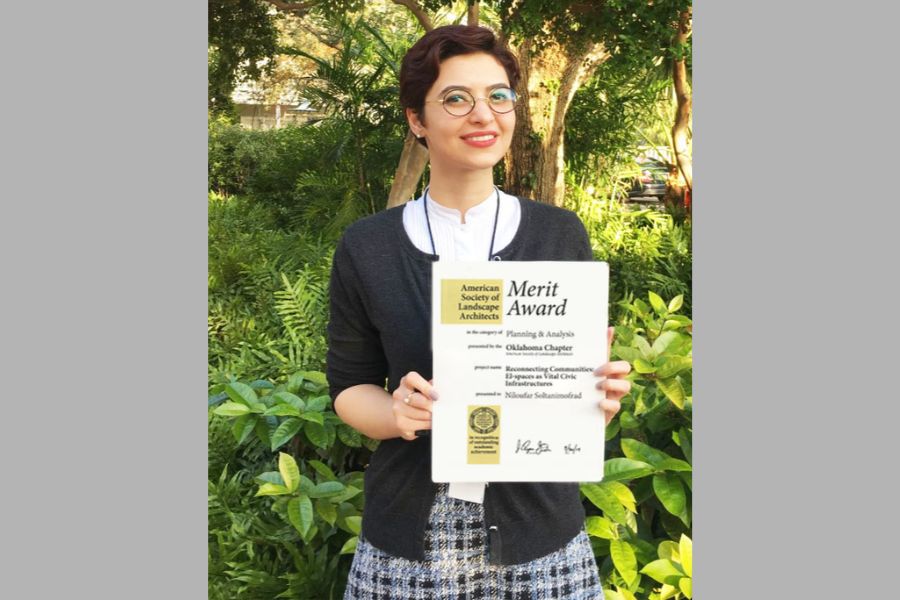 Niloufar Soltanimofrad standing in front of trees holding the Merit Award. 