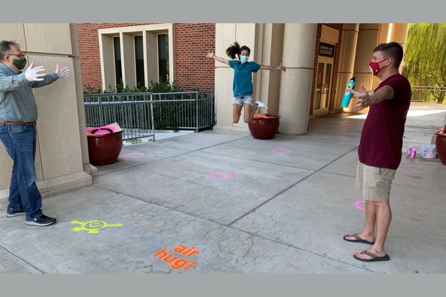 Three masked people spaced apart on painted sidewalk circles