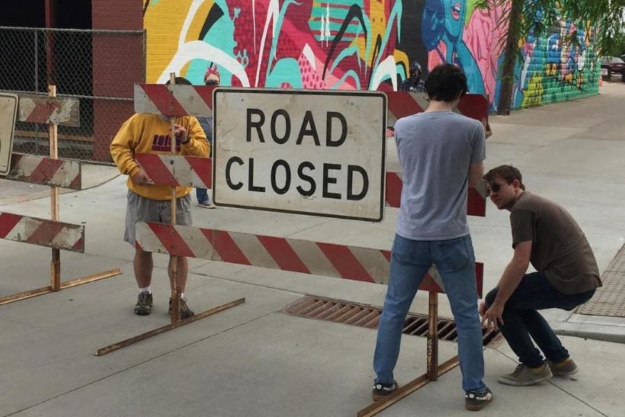 Three students moving a road closed sign with a mural in the background.