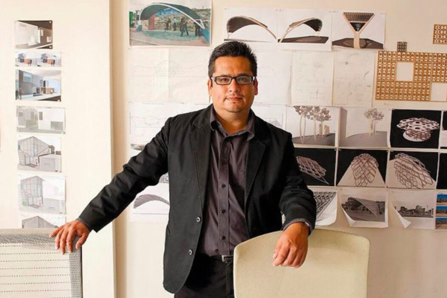 Rene Peralta standing in front of wall with architectural designs on wall in office.
