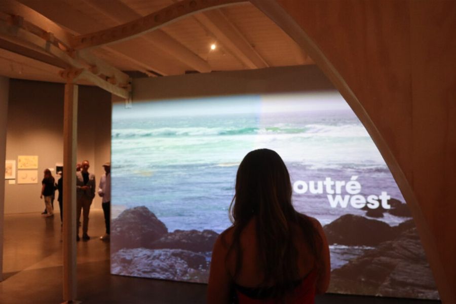 A guest stands in front of a projected image of the California coastline with the words "outré west" superimposed on it.