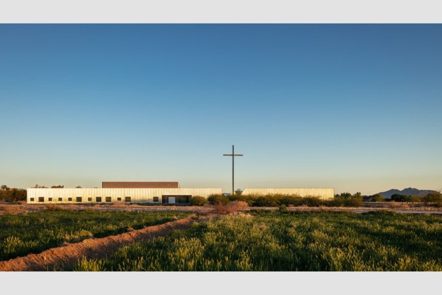 Exterior of a chapel designed by DeBartolo architects with crops in the foreground and mountains in the background.