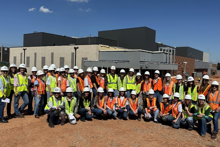 A group of Interior Design students with hardhats pose outside a construction site. 