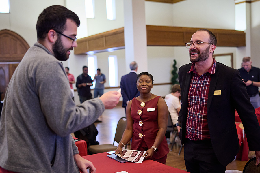 Graduate student at a resource fair with two volunteers providing information.