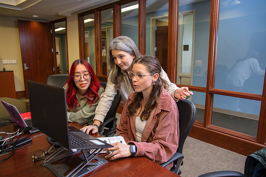 Graduate students around a computer inside the graduate study rooms.