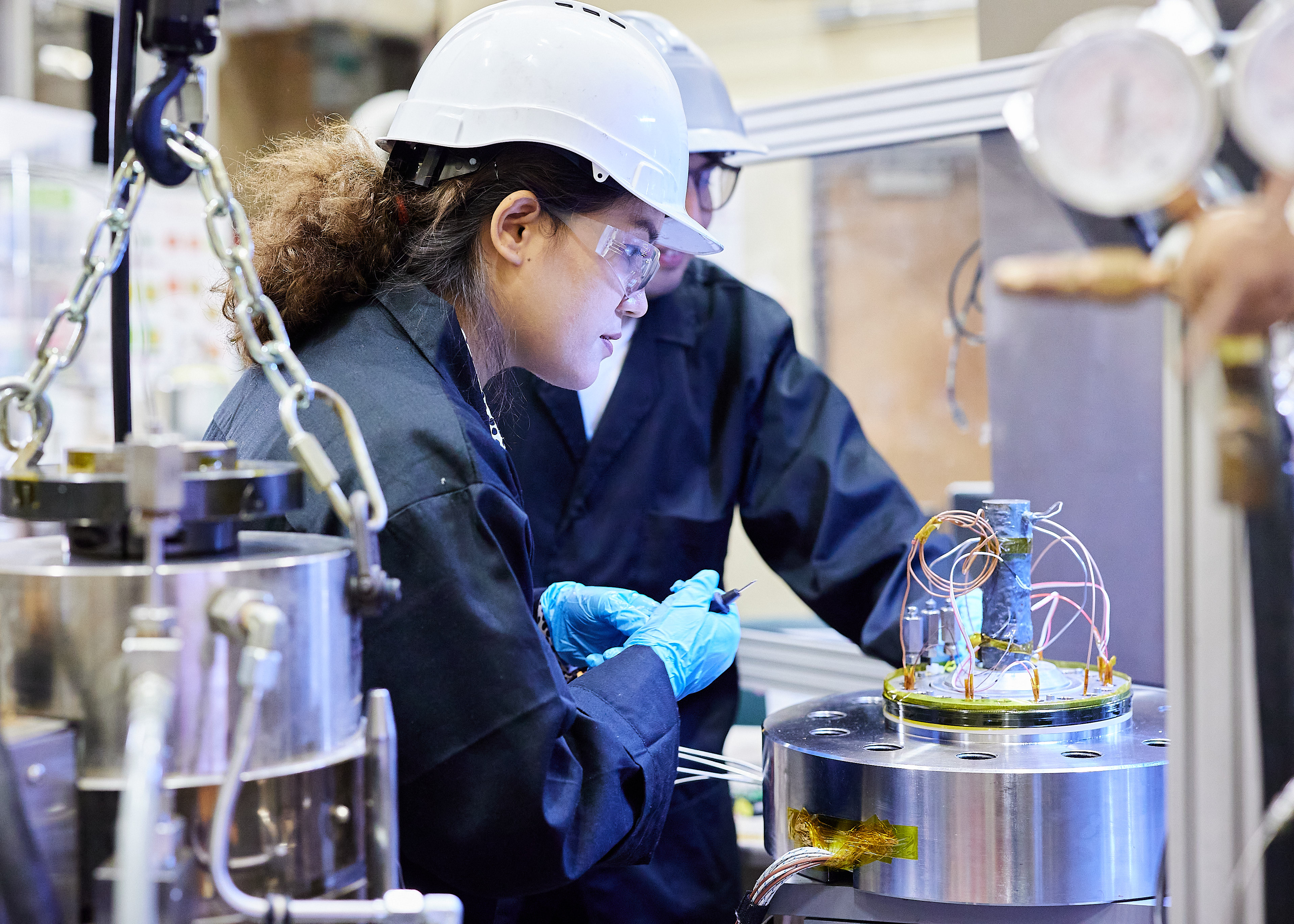 A scientist in a hardhat working with metal tools.