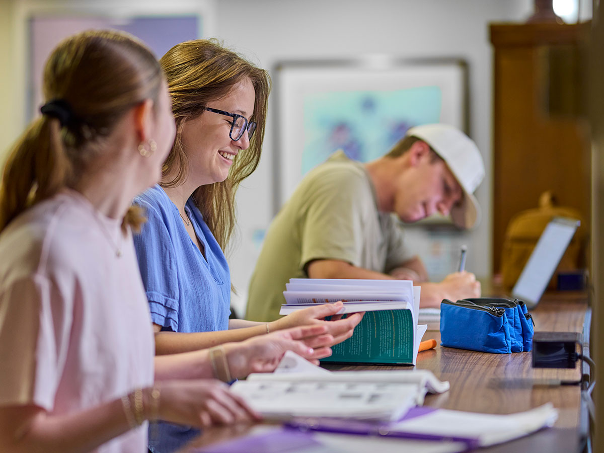 Three students work closely tegether at a workstation.