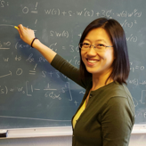 Professor Ying Wang, teaching at chalkboard, smiling at camera