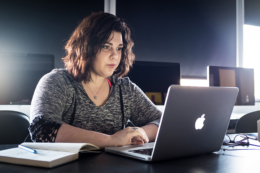 Woman studying from her laptop in a dimly lit room.