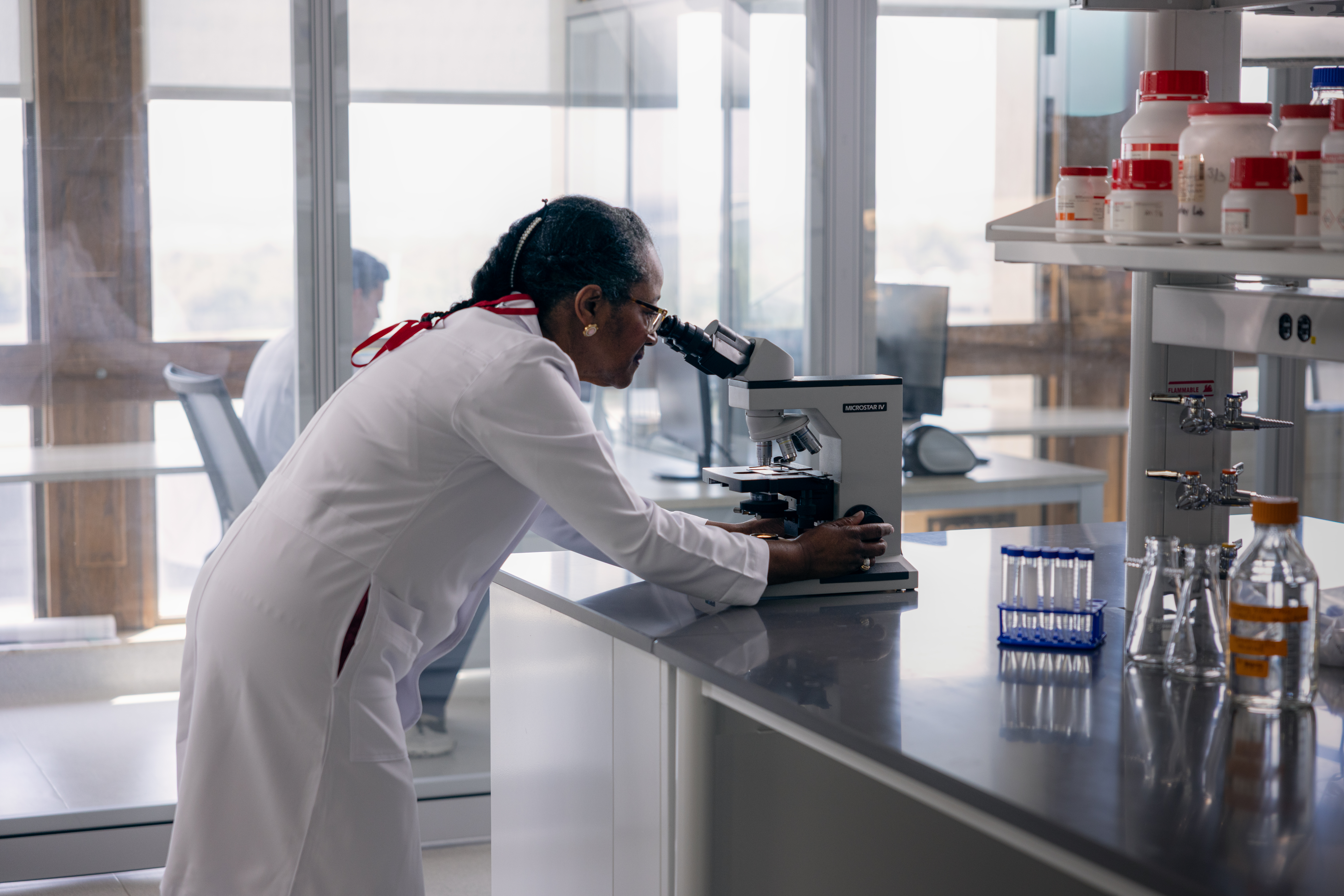 A person in a lab coat looking through a microscope.