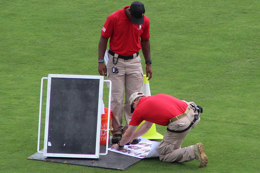 Two people in red shirts and khakis setting up a bullet trap in a grassy field.