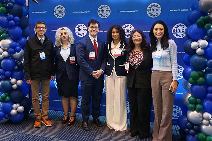 University students and faculty members pose in front of event backdrop.