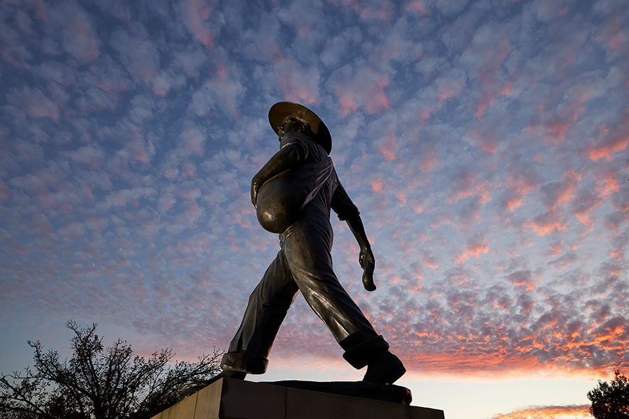 The OU Seed Sower statue captured at a low angle. The background in a sunset full of small clouds.